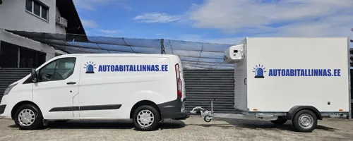 Autoabi Tallinnas tehnikakaubik ja kinnine järelhaagis logodega hoone ees, kaubiku akuriiulil on igal akul oma rihmaga kinnitatav pesa.